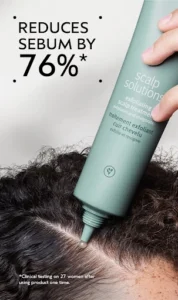 A person applies scalp exfoliant from a green bottle to their scalp; text reads “Reduces sebum by 76%*” with additional clinical testing details.